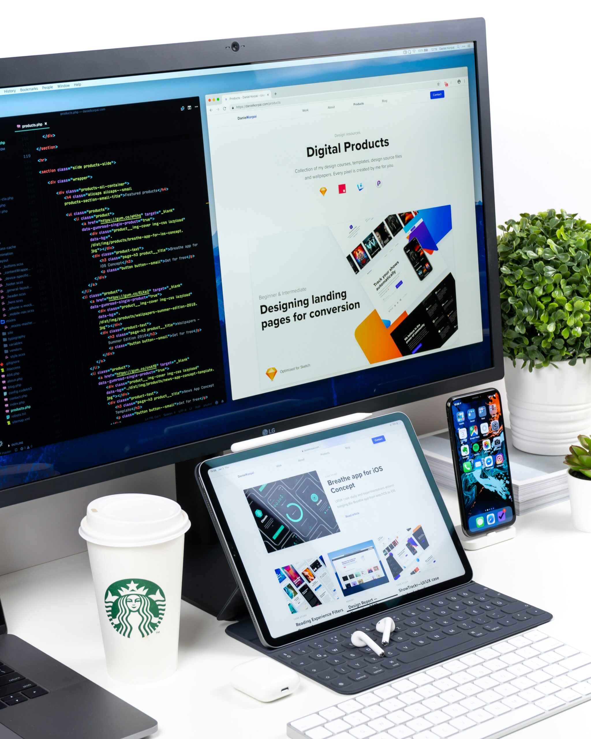 Modern software development workspace featuring a large monitor displaying web design and code, a tablet with a keyboard showing a mobile app interface, a smartphone on a stand, and accessories like a Starbucks coffee cup, AirPods, and a keyboard, all on a white desk with decorative plants.